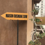 Panneau d'indication jaune avec Maison Ousmane Son écrit en noir